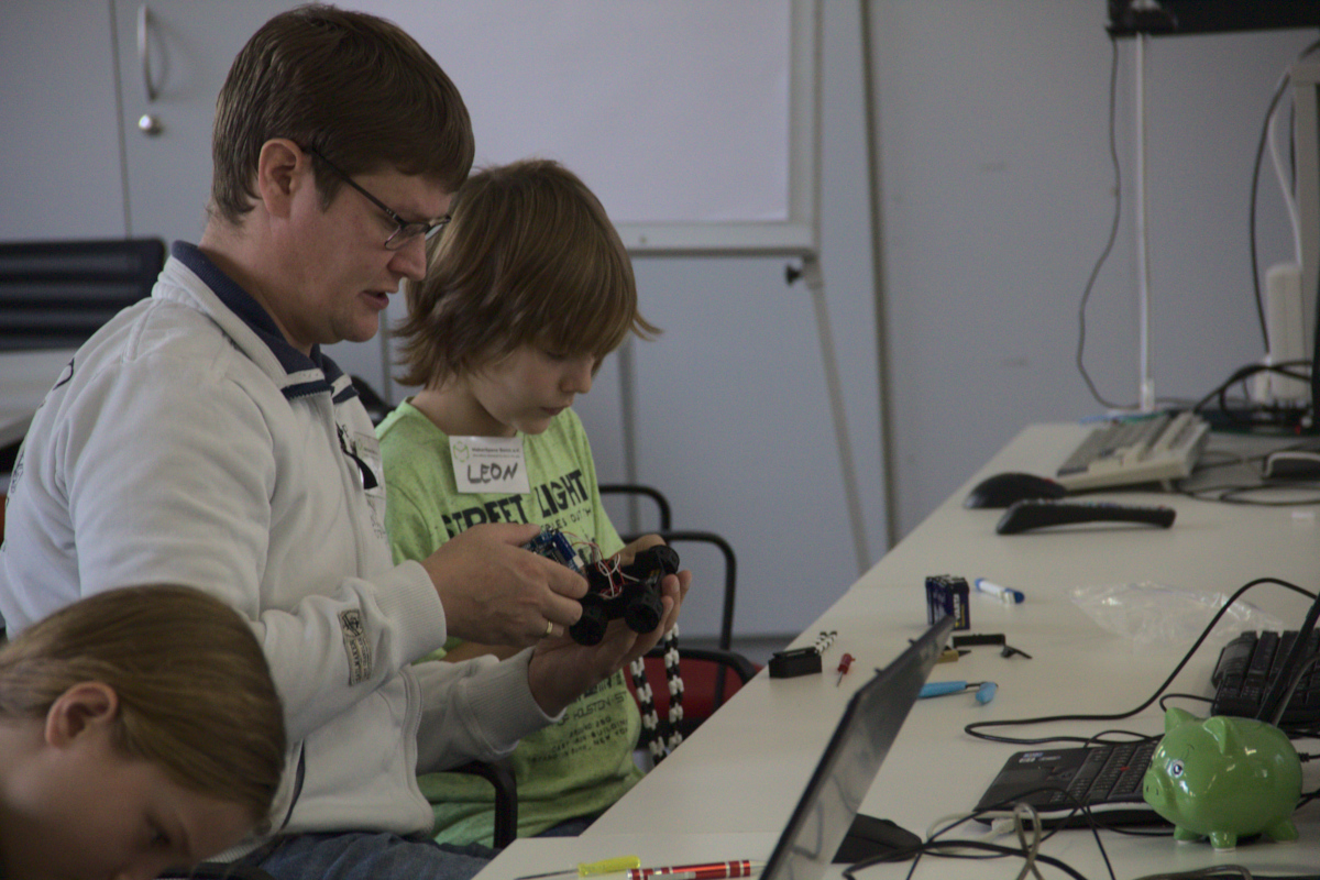 Ein Mann und ein Junge basteln im Makerspace gemeinsam an einem kleinen, programmierbaren Auto