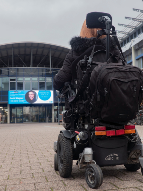 Studentin Karolin Odenthal in ihrem Rollstuhl auf dem Weg zum Haupteingang der Hochschule